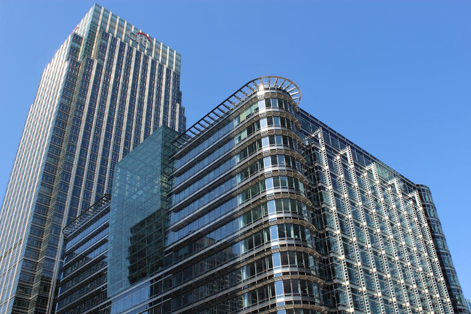 A modern commercial building in Canary Wharf with reflective glass windows and a distinctive curved architectural feature near the water's edge. The scene is set during daylight with overcast skies, c